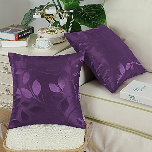 Purple satin cushions on a sofa with a decorative lamp and books nearby.