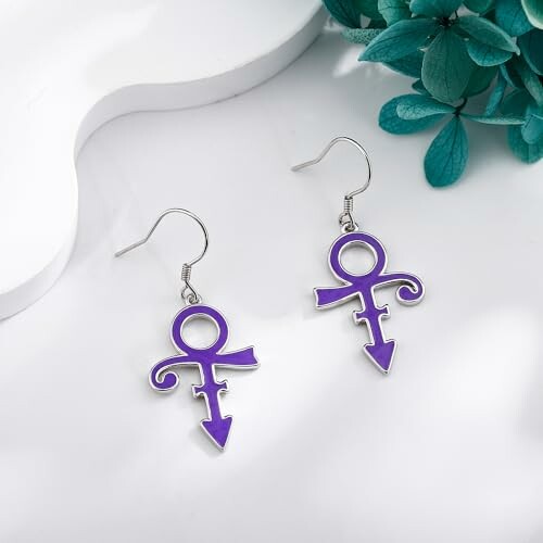 Purple symbol earrings on white surface with green leaves