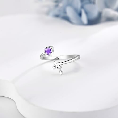 Silver ring with a purple heart and symbol design on a soft background.